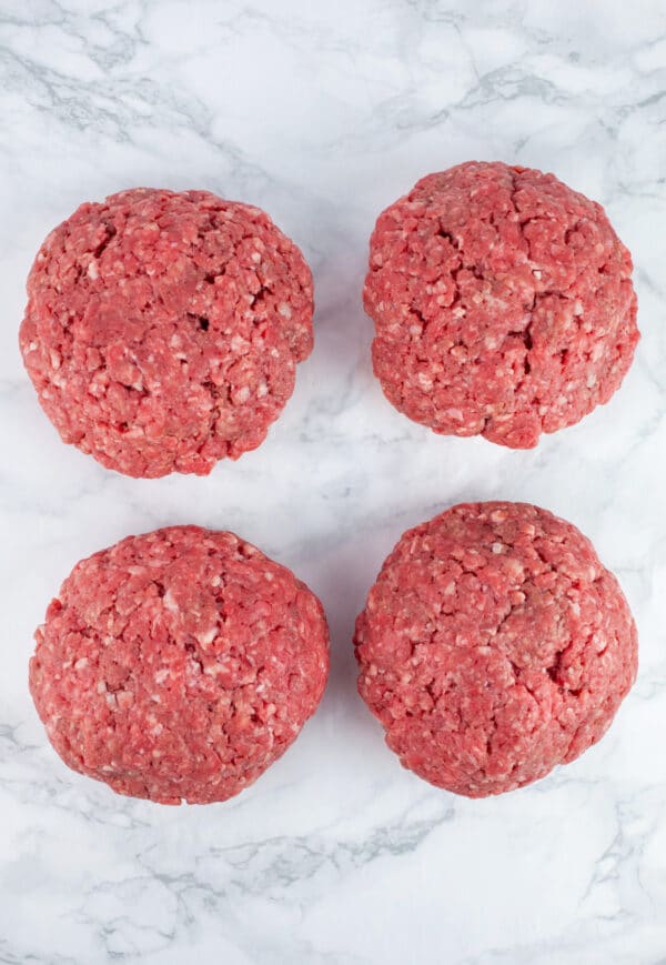 Raw beef burger patties on white surface.