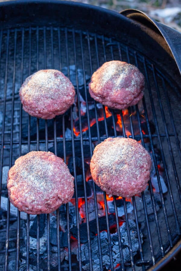 Uncooked ground beef burgers on charcoal grill.