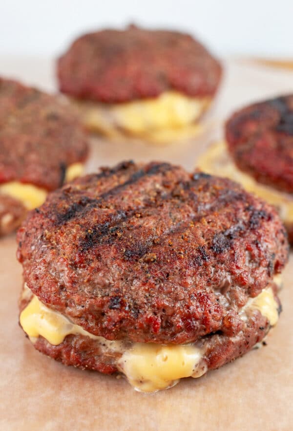 Juicy Lucy burger patty with cheese melting out of the sides on wooden serving board.