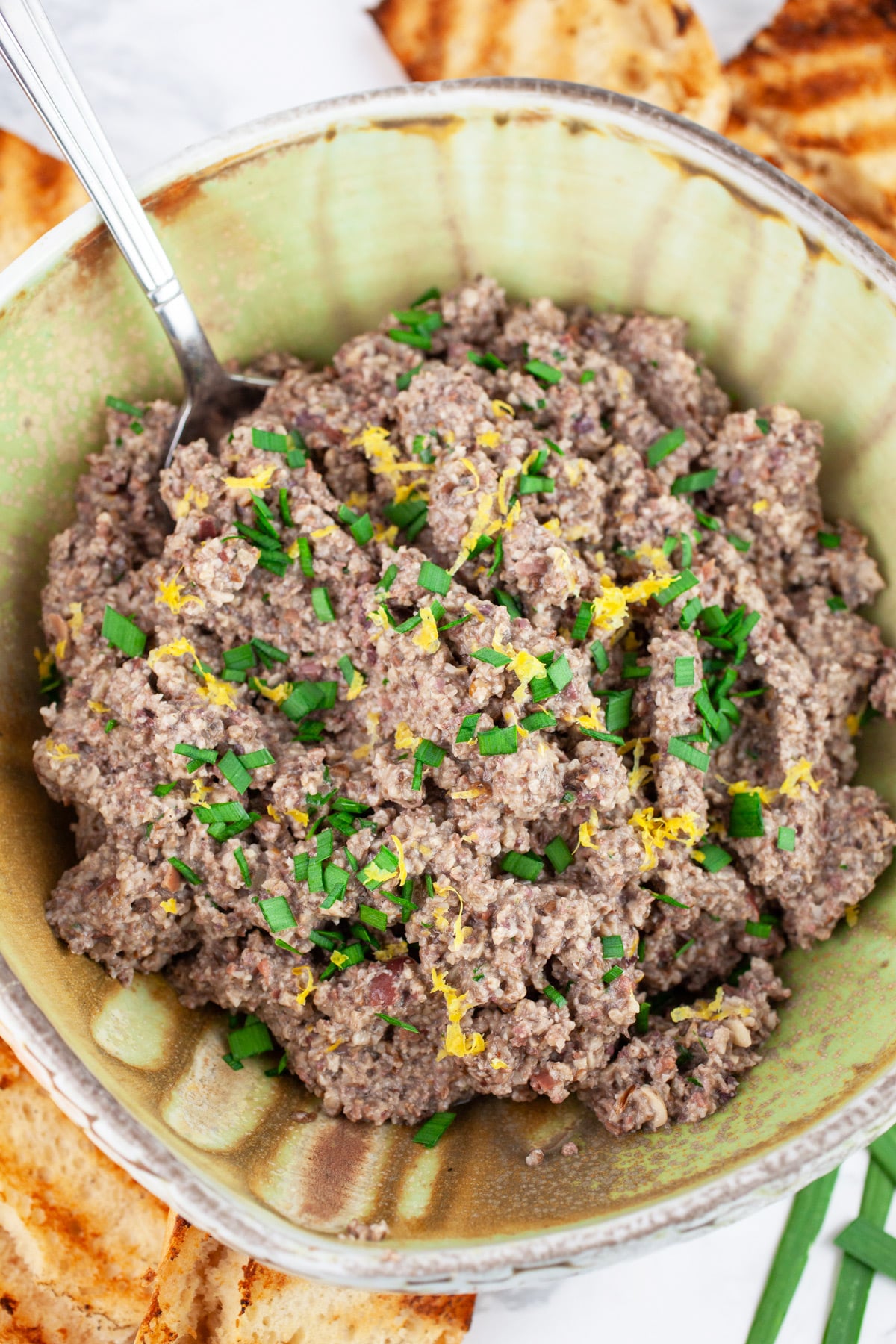 Mushroom tapenade in ceramic bowl with spoon next to slices of grilled bread.