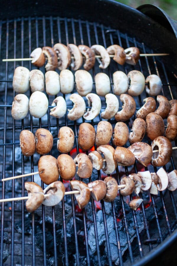 Mushroom skewers cooking on charcoal grill.