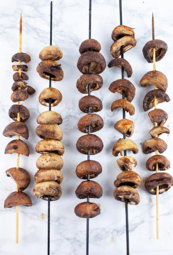 Cooked mushroom on skewers on white surface.