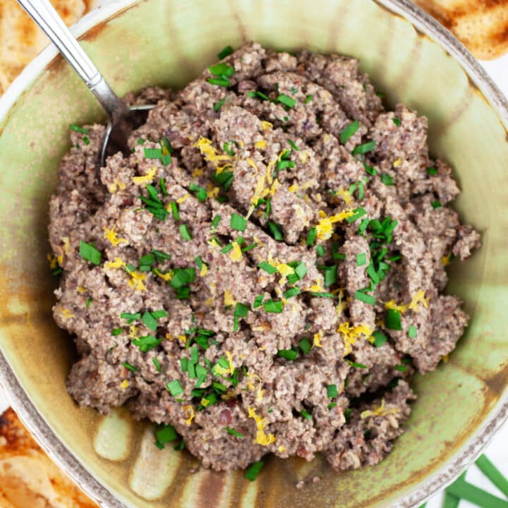 Mushroom tapenade garnished with minced chives and lemon zest in ceramic bowl with spoon.