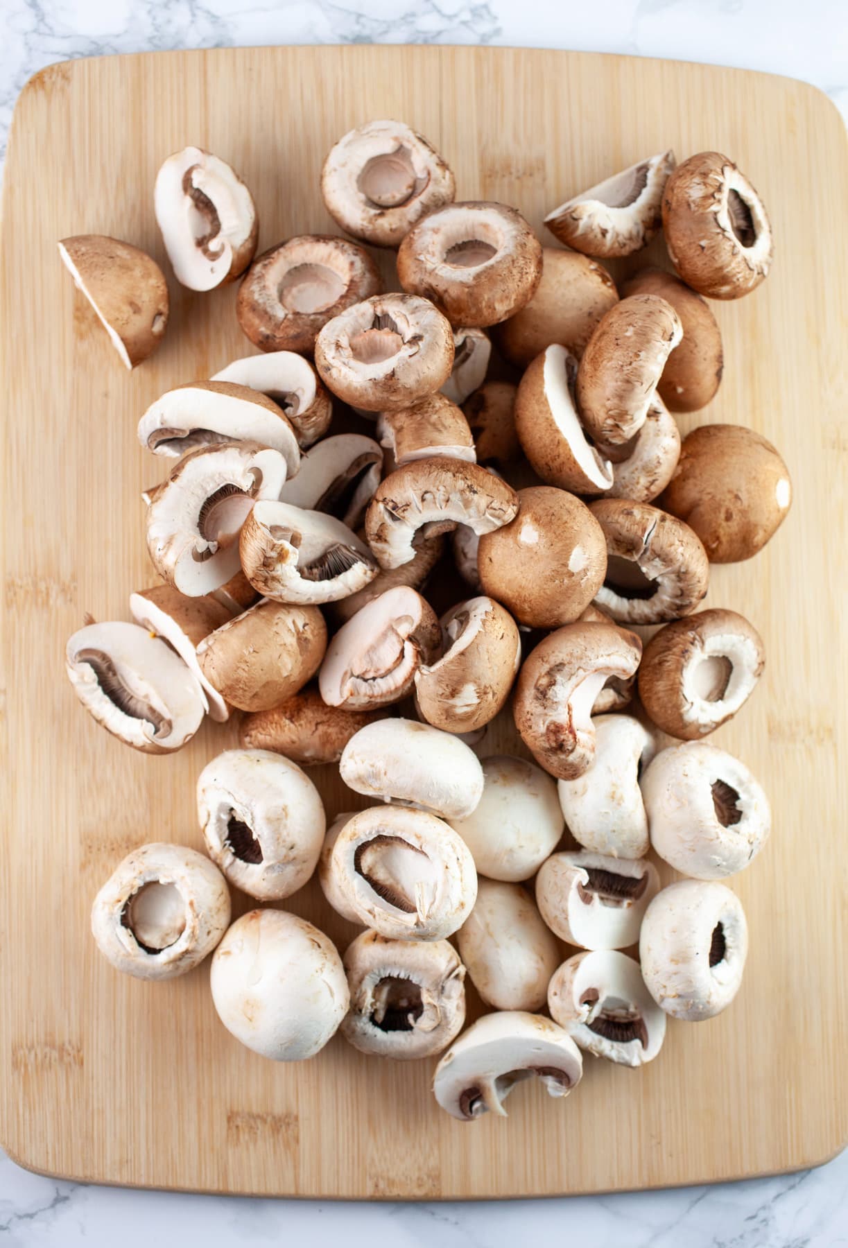 Whole cremini and white button mushrooms on wooden cutting board.