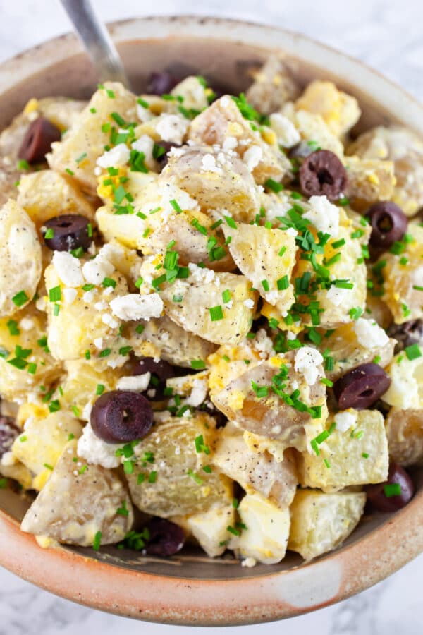 Mediterranean potato salad garnished with fresh chives in ceramic bowl with spoon.