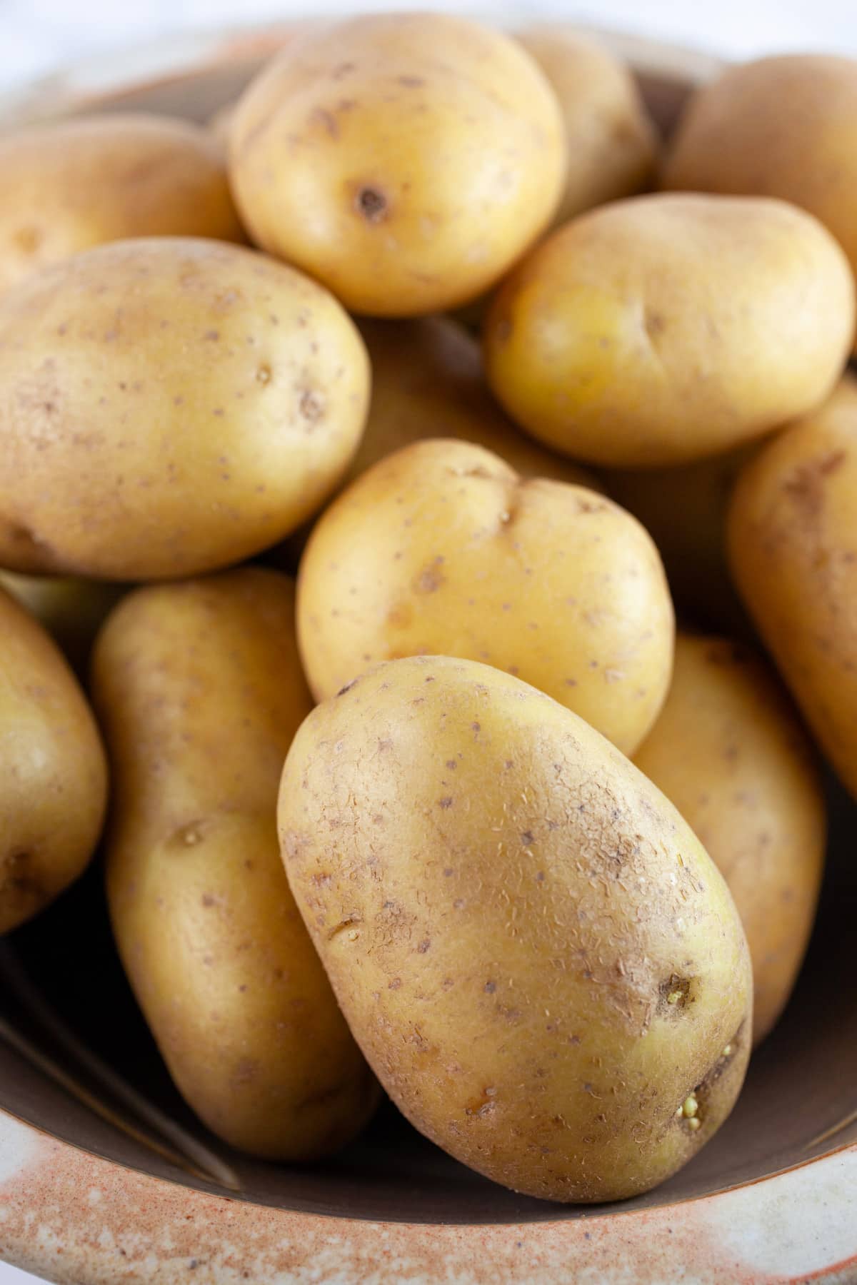 Whole, uncooked Yukon gold potatoes in ceramic bowl.