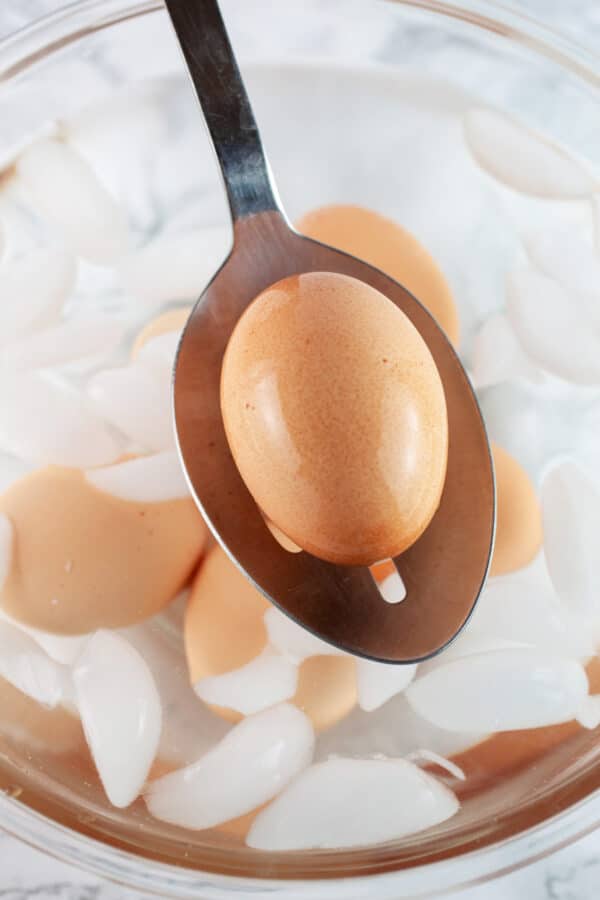 Hard boiled egg lifted from ice bath on metal ladle.