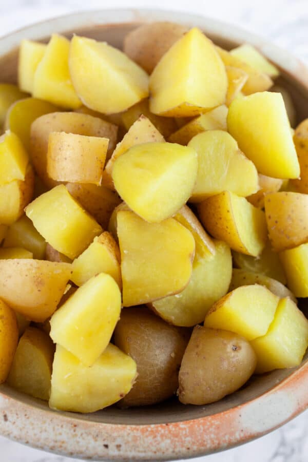 Diced, cooked yellow potatoes in ceramic bowl.