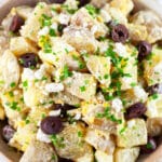 Mediterranean potato salad with feta cheese, Kalamata olives, and chives in ceramic bowl.