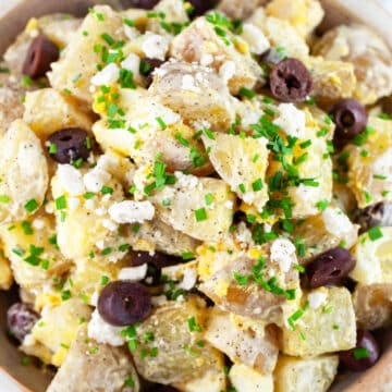 Mediterranean potato salad with feta cheese, Kalamata olives, and chives in ceramic bowl.