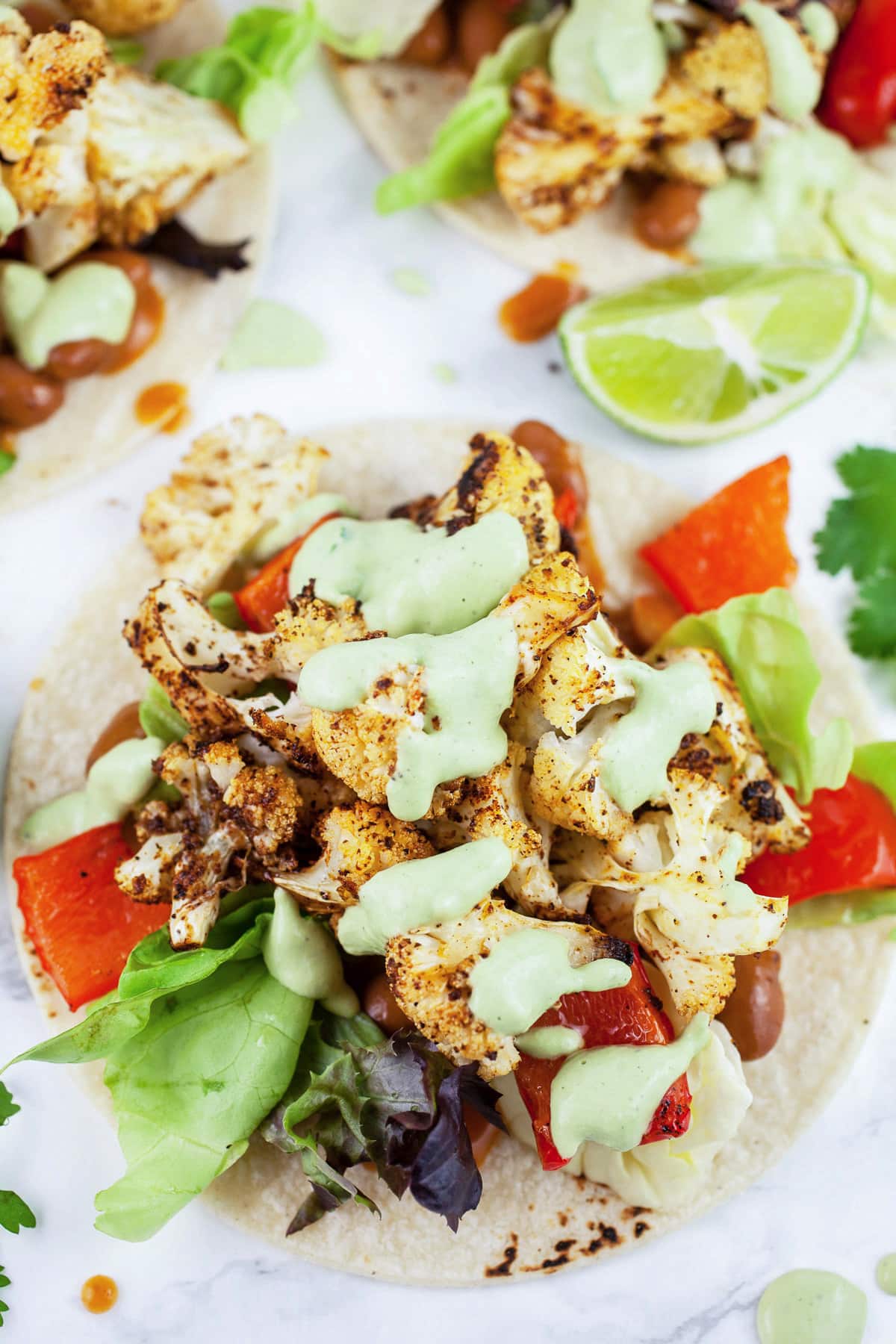 These Easy Roasted Veggie Tacos make the best quick and healthy dinner recipe! These tacos are vegetarian and gluten free. They're full of roasted zucchini, bell peppers, and black beans and topped with Queso Fresco cheese. The perfect meal for Meatless Monday! #tacos #veggie #vegetarian #roasted #glutenfree Roasted veggie tacos topped with cashew cilantro sauce.