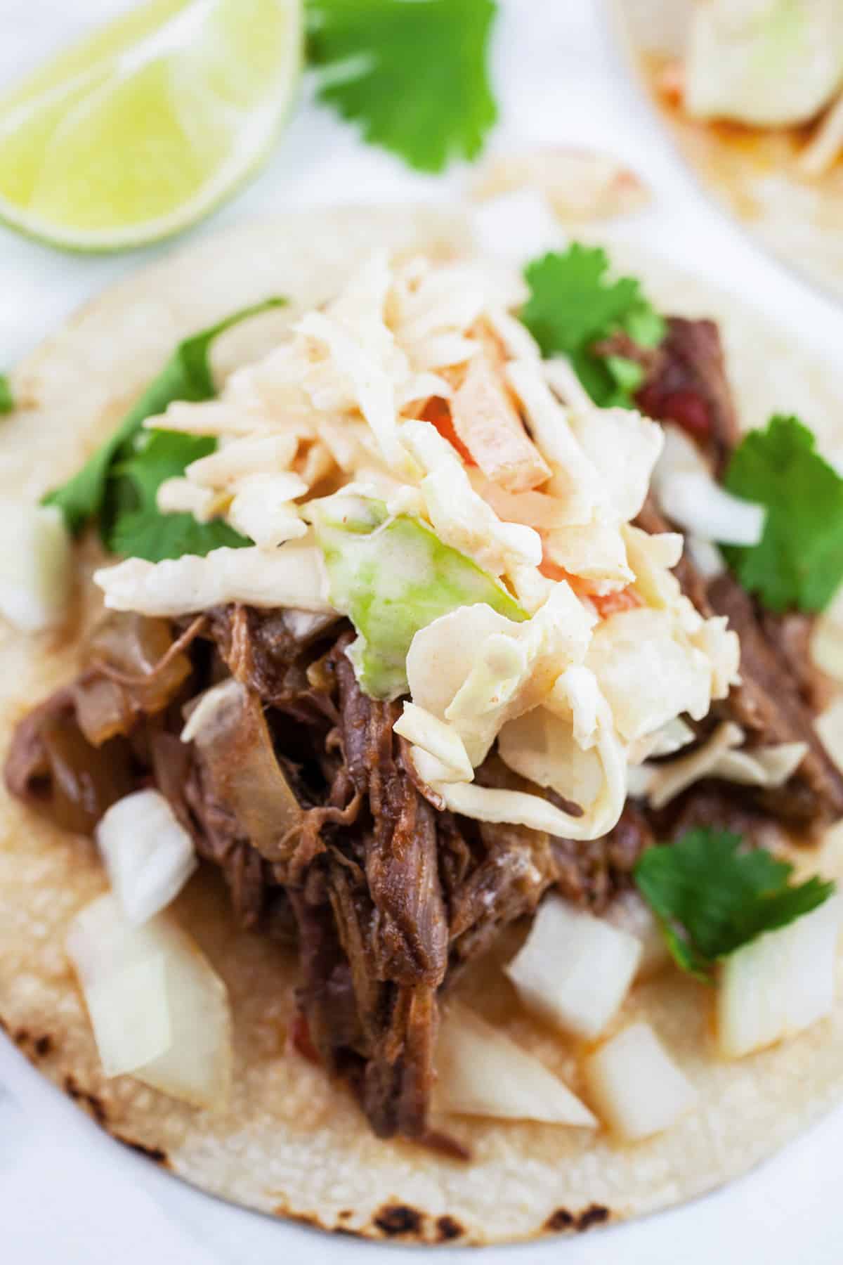 Barbacoa tacos with chipotle slaw on corn tortillas with diced onions, cilantro, and lime wedges.