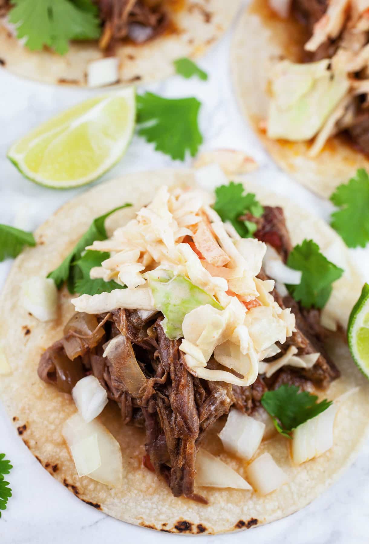Shredded barbacoa tacos on corn tortillas with chipotle slaw, diced onions, cilantro, and lime wedges.