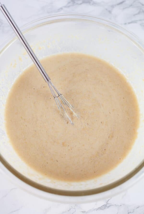 Tahini paste with water and lemon juice in glass bowl with small whisk.