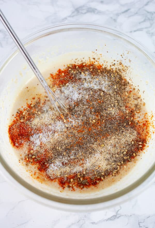 Tahini with spices in glass bowl with small whisk.