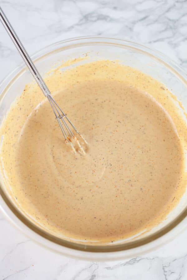 Harissa tahini sauce in glass bowl with small whisk.