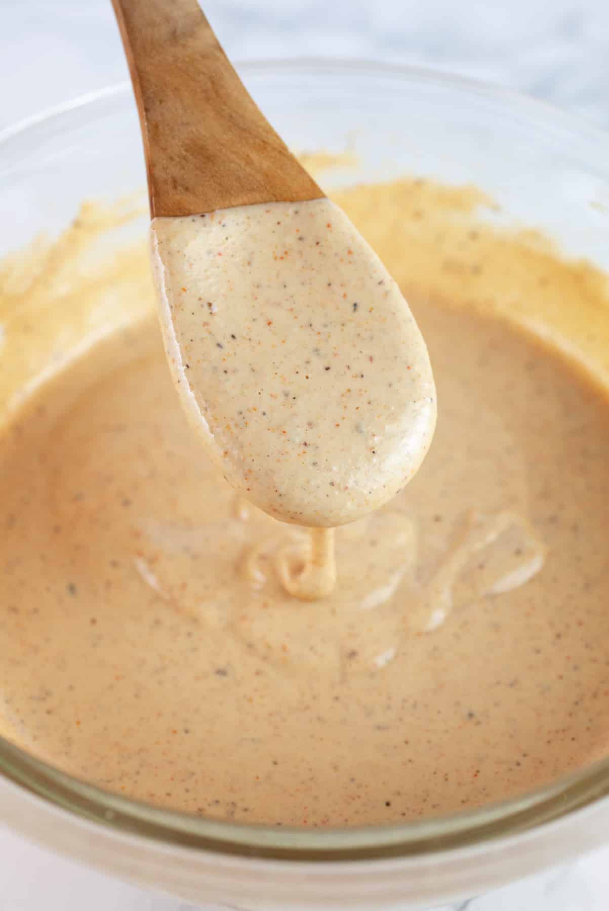 Wooden spoonful of harissa tahini sauce lifted from glass bowl.