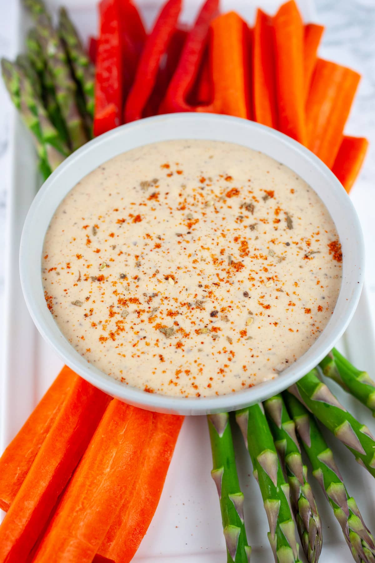 Harissa tahini sauce on white platter with raw vegetables.