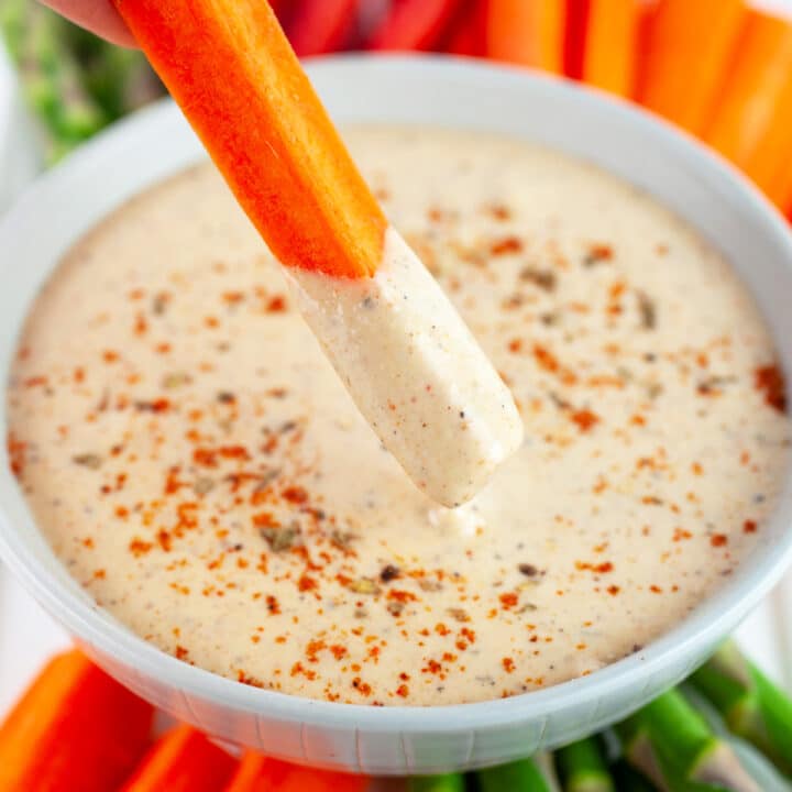 Carrot stick dipped into bowl of harissa tahini sauce with vegetable platter.
