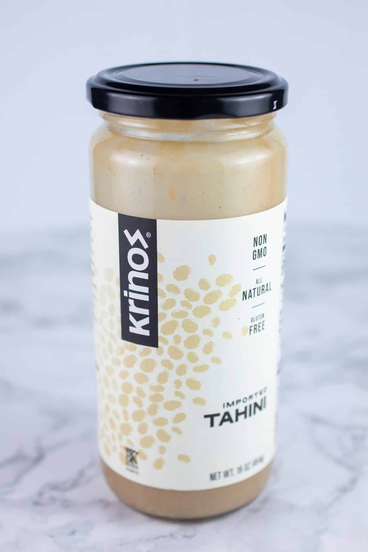Jar of tahini paste on white surface.