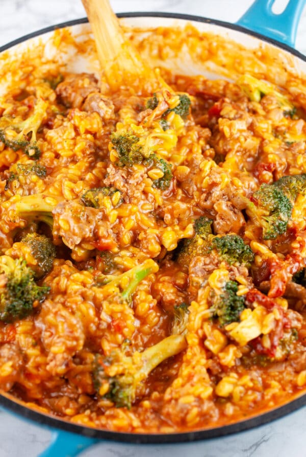 Cooked sausage broccoli pasta in skillet with wooden spoon.