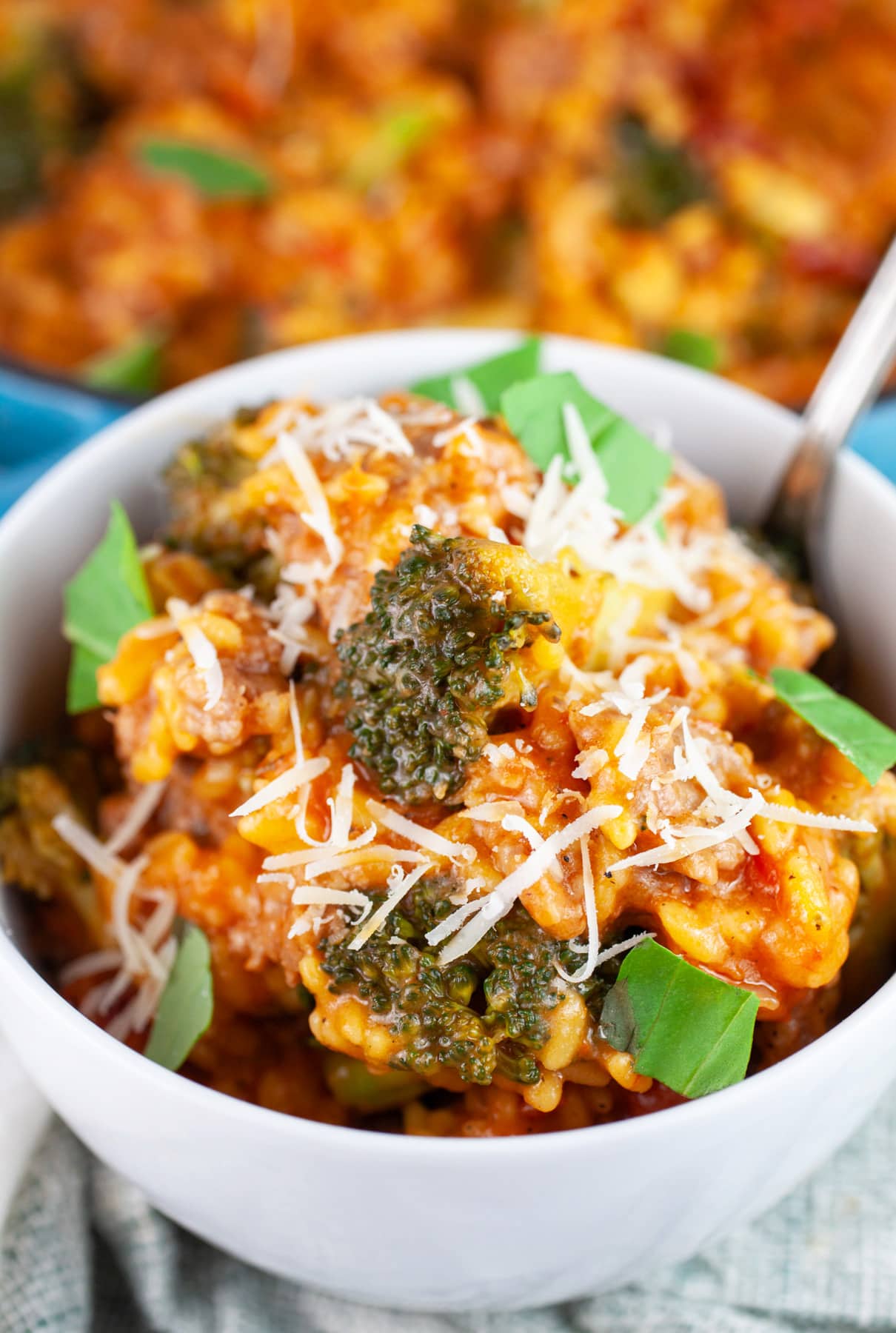 Broccoli sausage pasta garnished with Parmesan cheese and fresh basil in white bowl with fork.