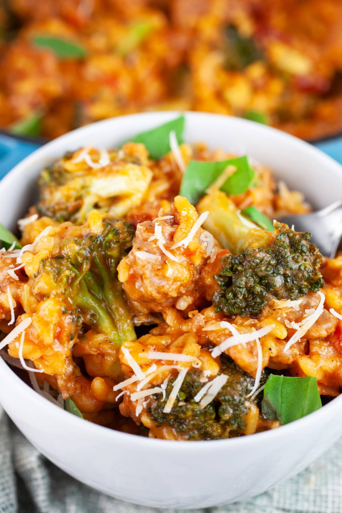 Sausage broccoli pasta garnished with Parmesan cheese and fresh basil in white bowl with fork.