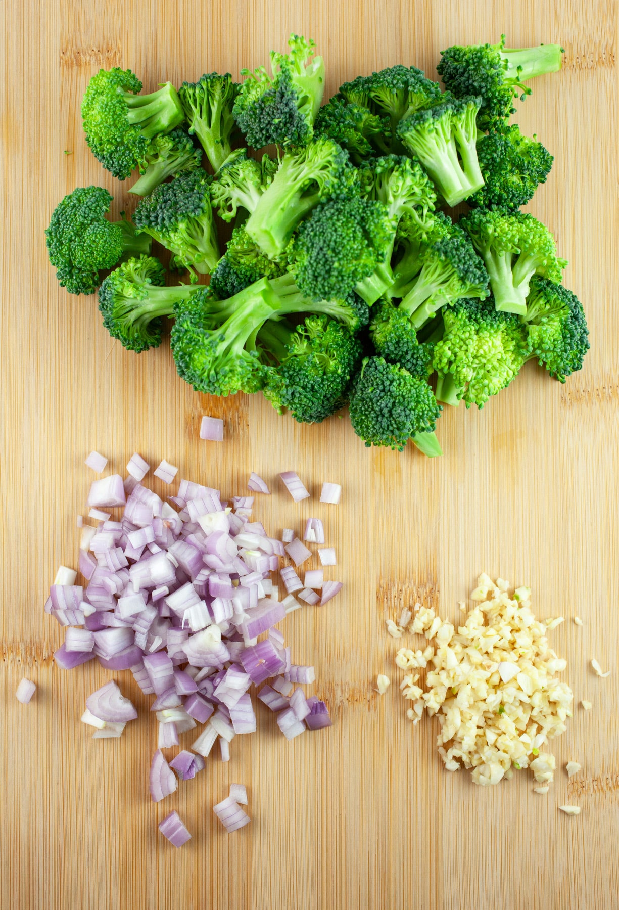 Minced garlic, shallots, and broccoli florets on wooden cutting board.