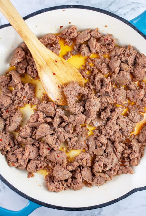 Cooked ground Italian sausage in skillet with wooden spoon.