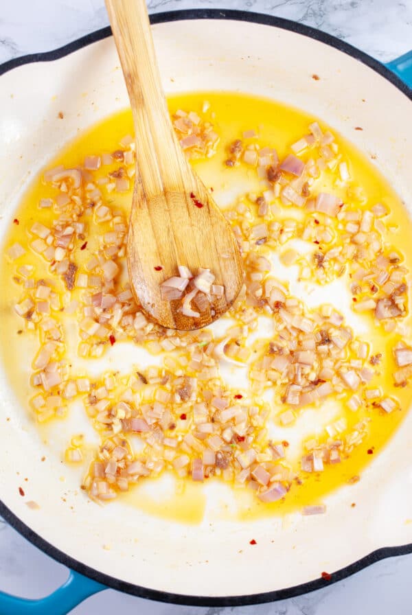 Garlic and shallots cooked in skillet with wooden spoon.