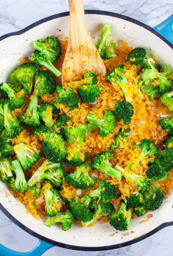 Broccoli florets and orzo pasta sauteed in skillet with wooden spoon.