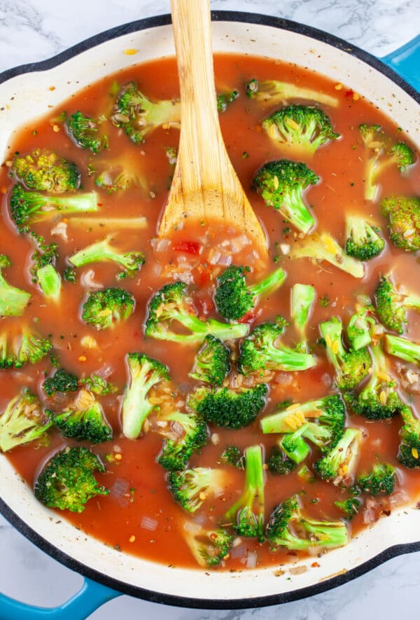 Broccoli and orzo pasta cooked in tomato broth in skillet with wooden spoon.