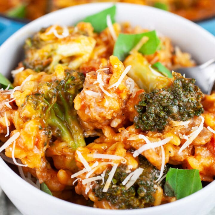 Sausage broccoli pasta garnished with Parmesan cheese and basil in white bowl.