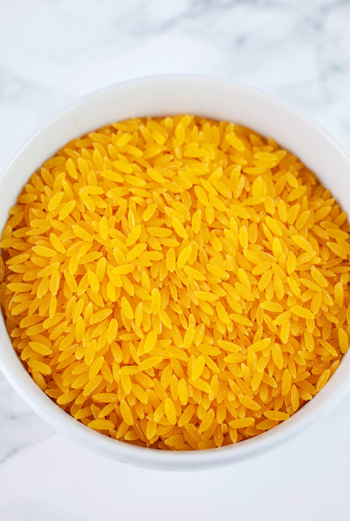 Uncooked gluten free orzo pasta in small white bowl.