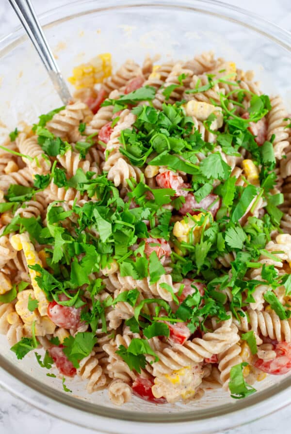 Minced cilantro added to Southwest pasta salad in large glass mixing bowl.
