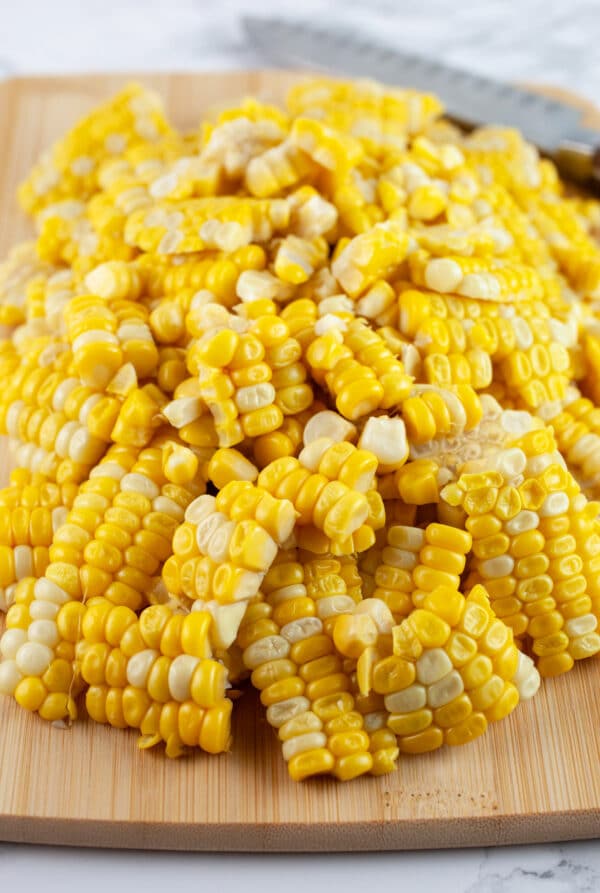 Cooked sweet corn kernels on wooden cutting board with knife.
