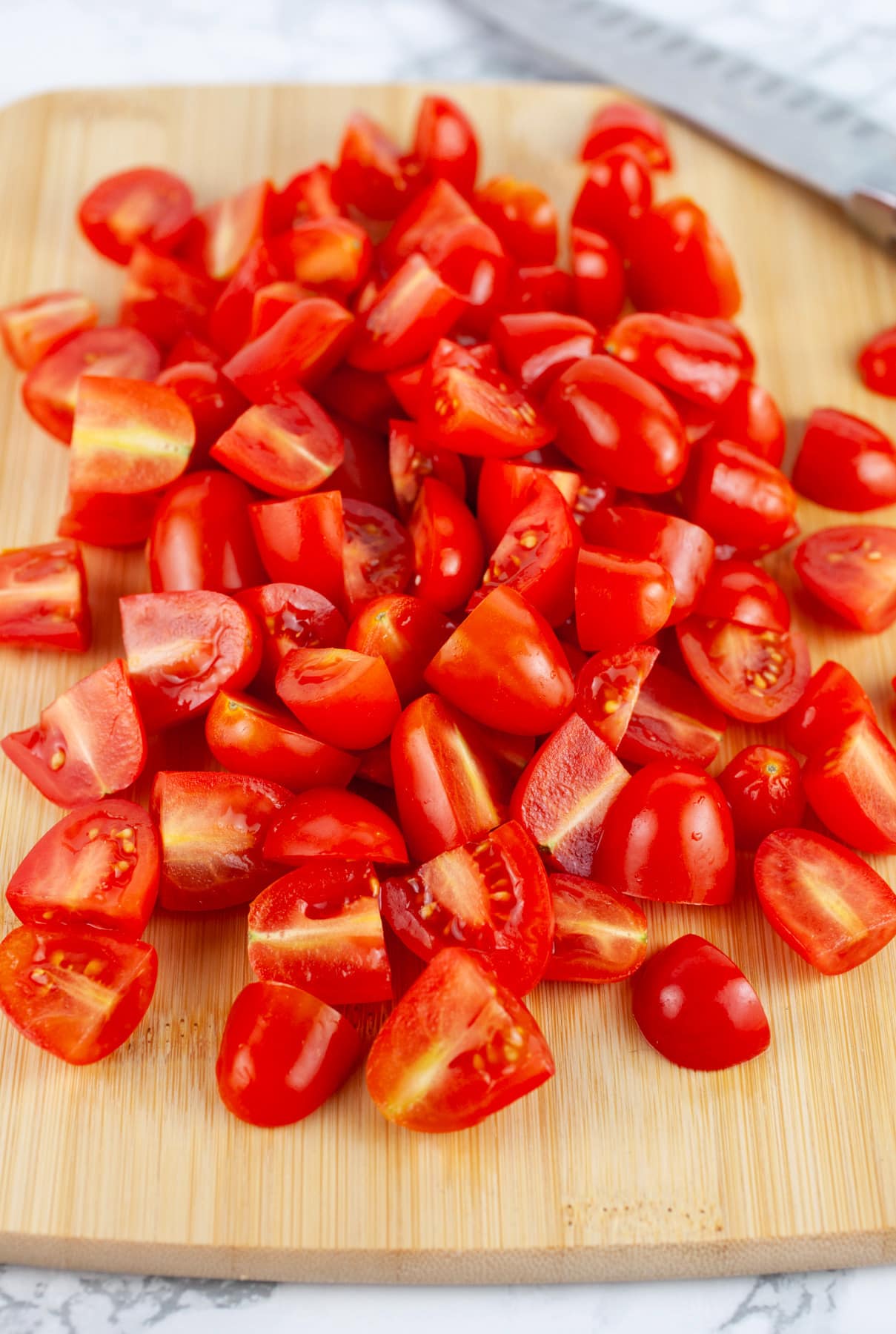 Chopped grape tomatoes on wooden cutting board with knife.