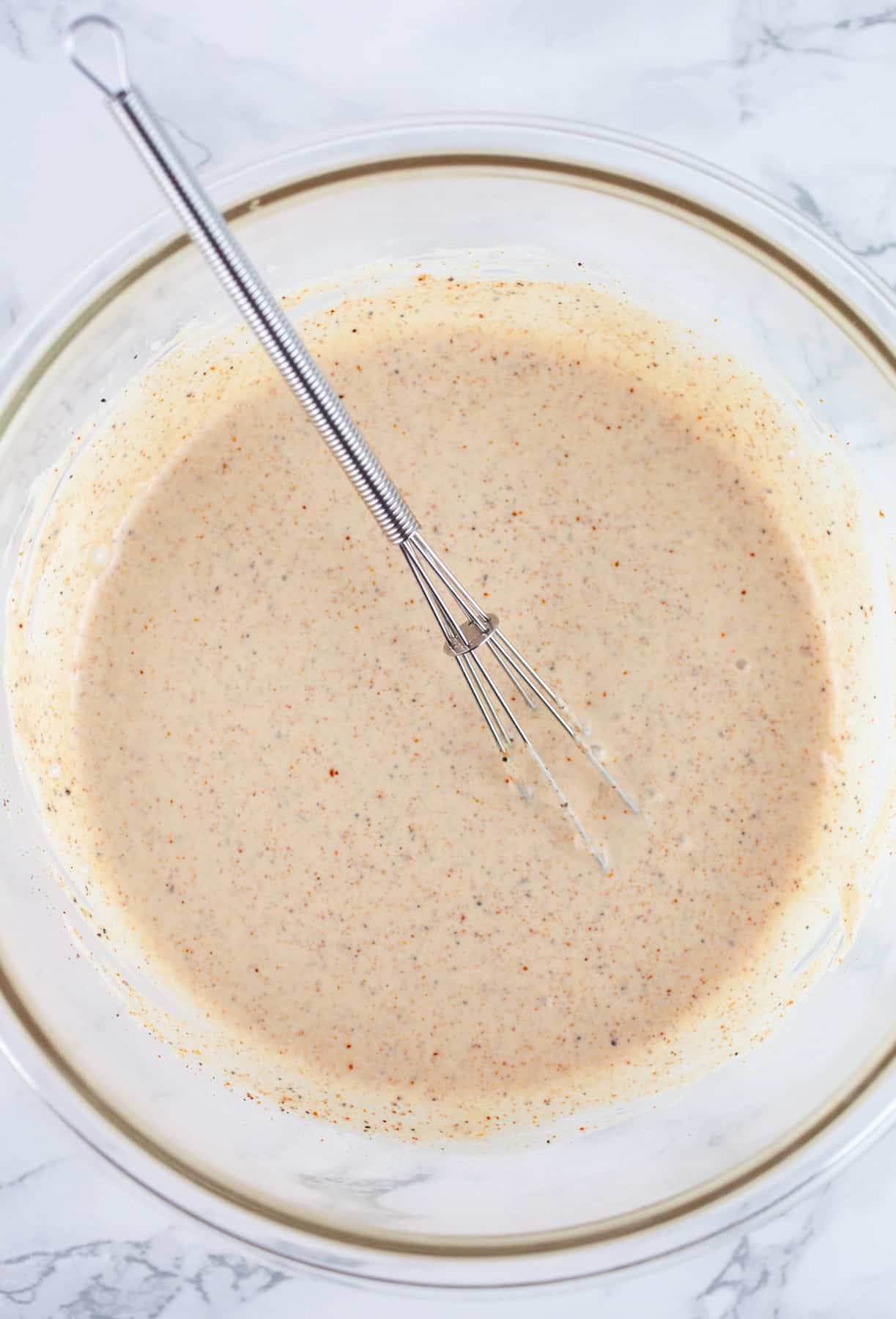 Creamy chili lime dressing in glass bowl with small whisk.