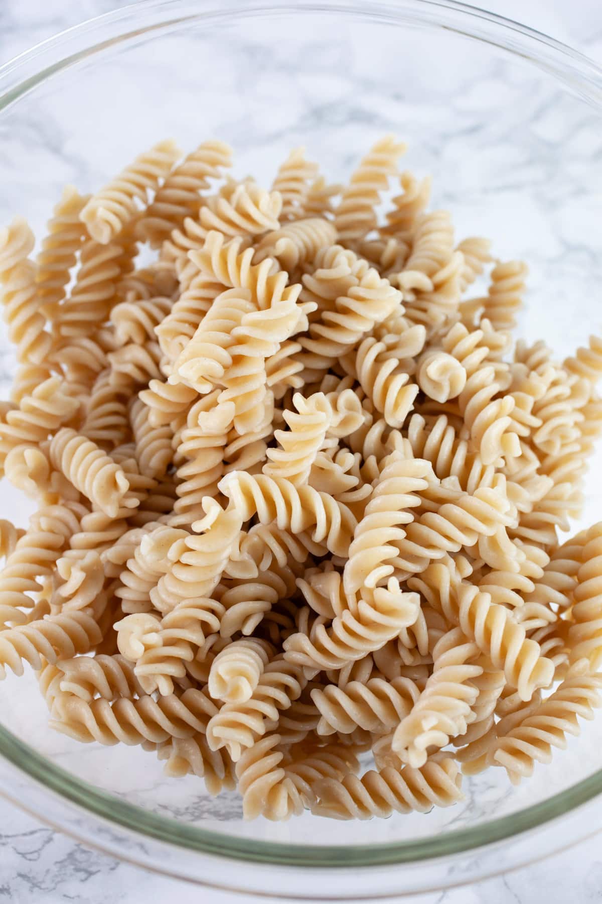 Cooked gluten free fusilli noodles in large glass bowl.