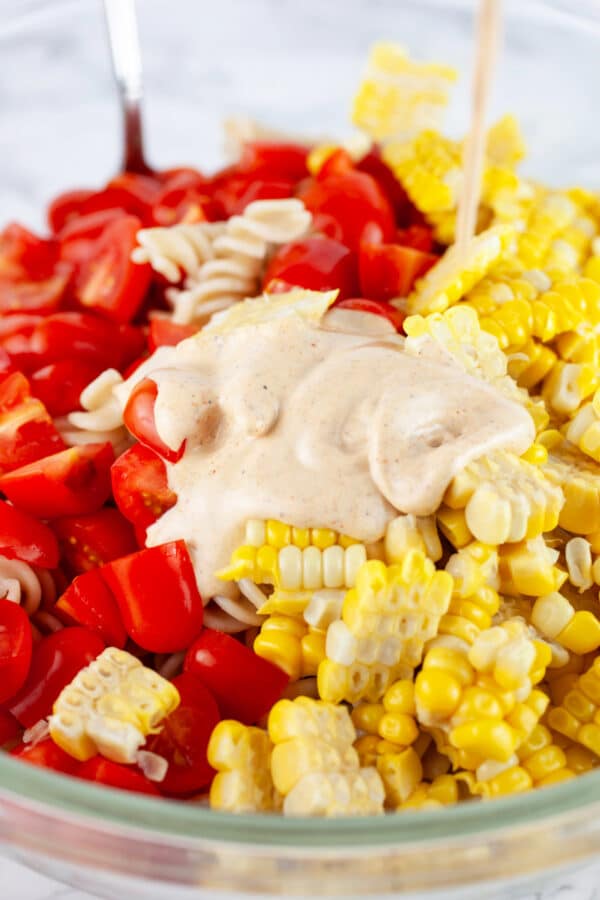 Chili lime dressing poured over corn and tomato pasta salad in large glass bowl.