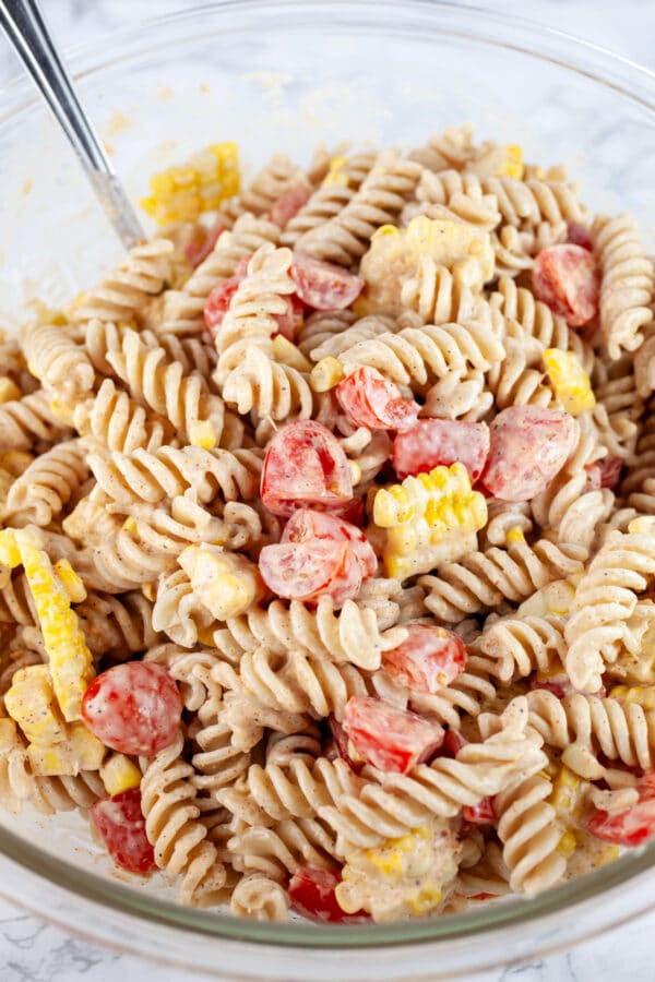 Southwest corn and tomato pasta salad mixed together in large glass bowl.