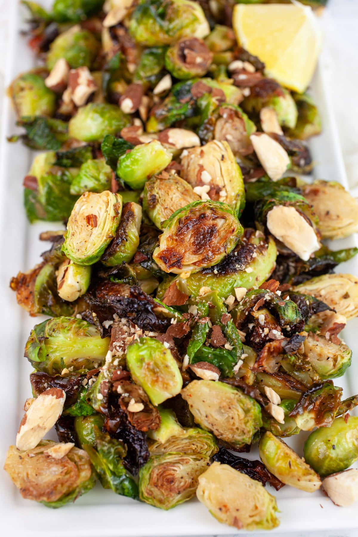 Maple mustard Brussels sprouts on white serving platter with almonds and lemon wedge.