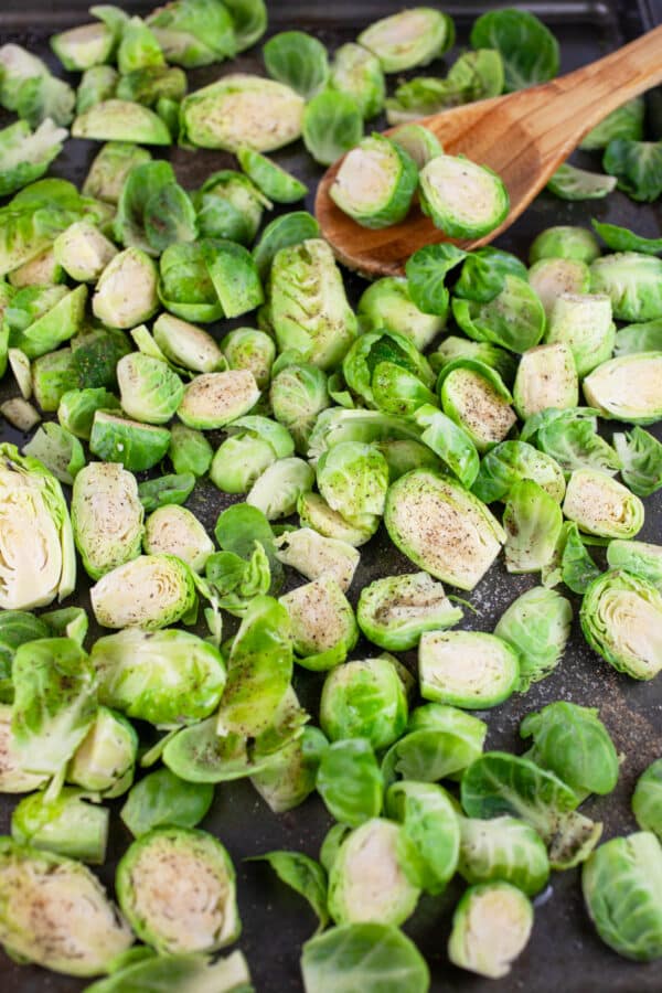 Uncooked Brussels sprouts on baking sheet with wooden spoon.