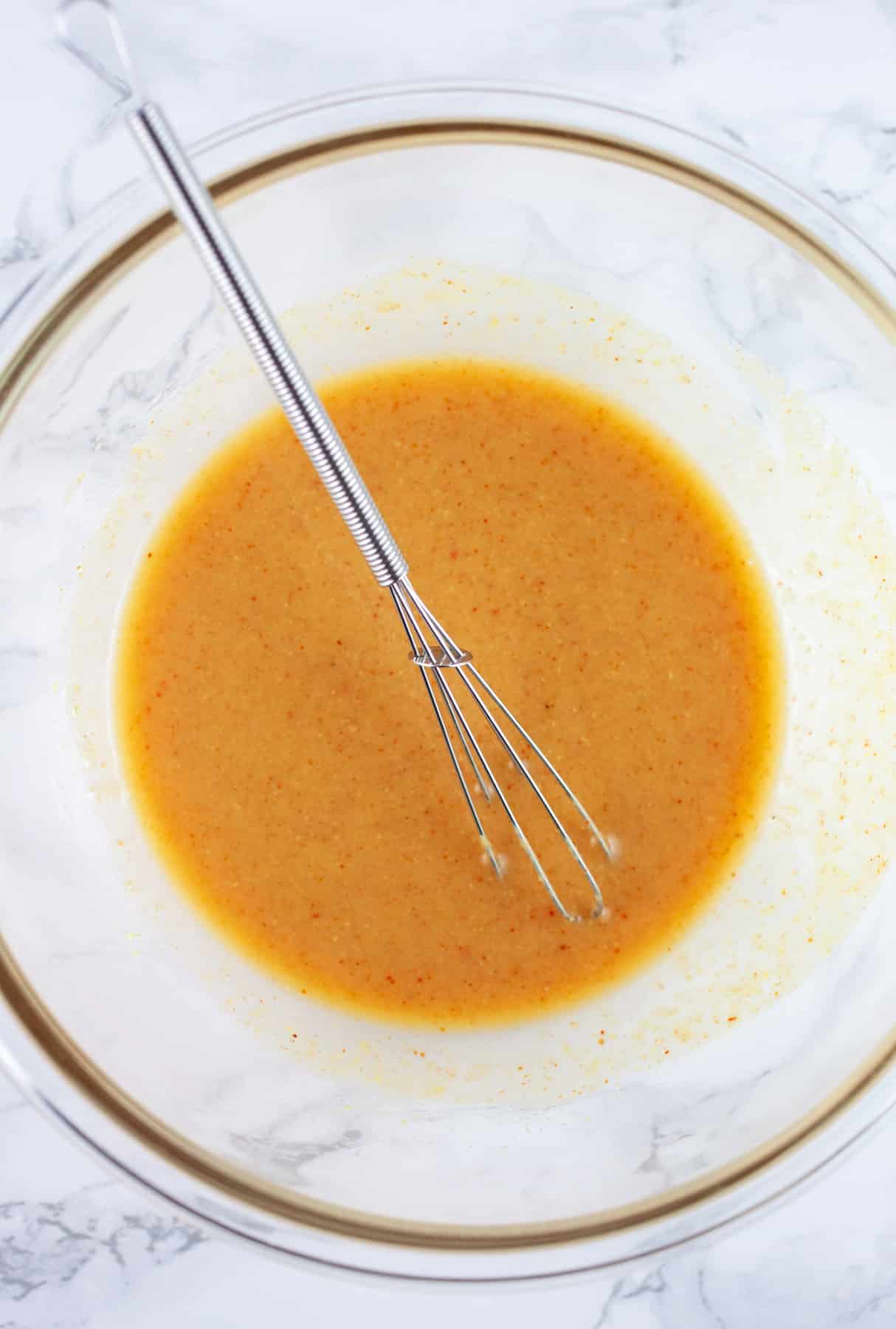 Maple mustard glaze in glass bowl with small whisk.