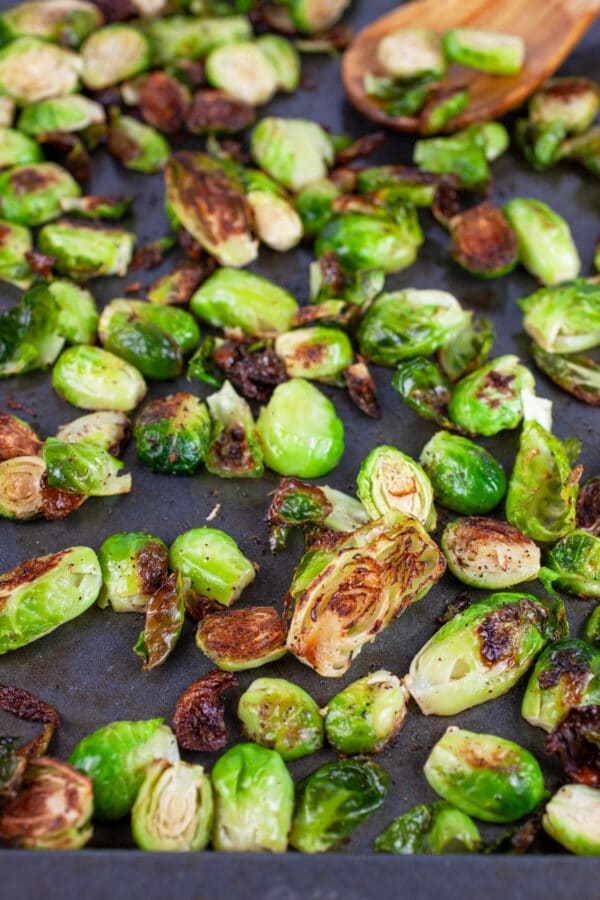 Roasted Brussels sprouts on baking sheet with wooden spoon.