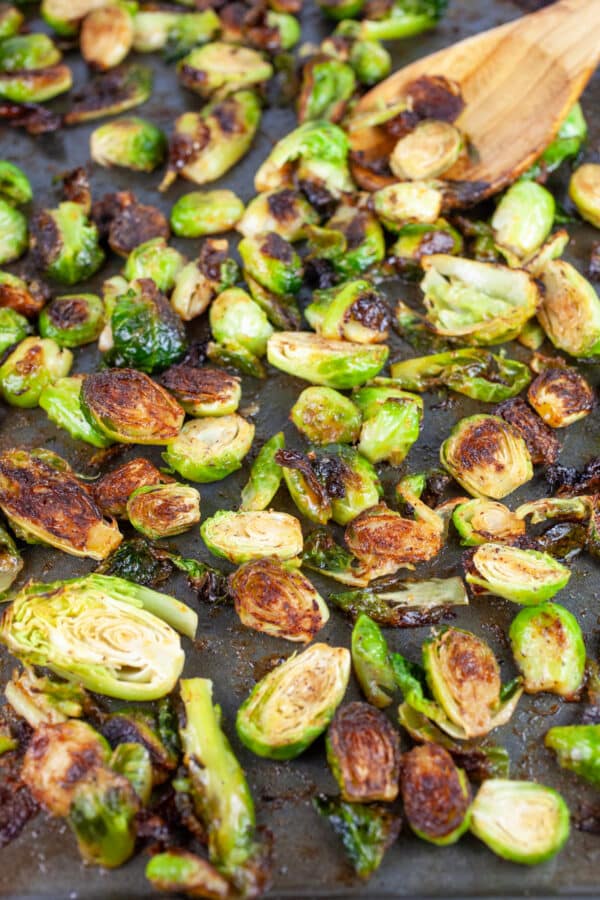 Glazed and roasted Brussels sprouts on baking sheet with wooden spoon.