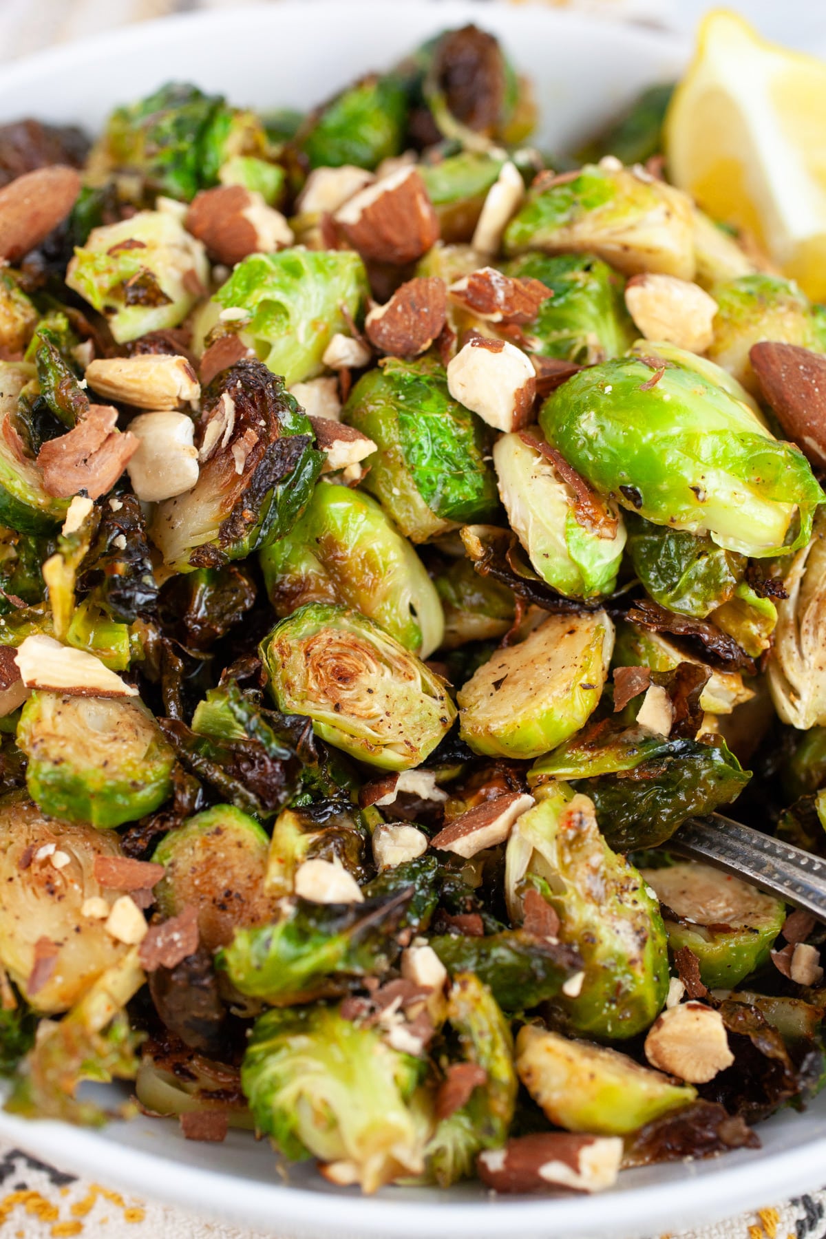 Roasted maple mustard Brussels sprouts with almonds and lemon wedge in white bowl.
