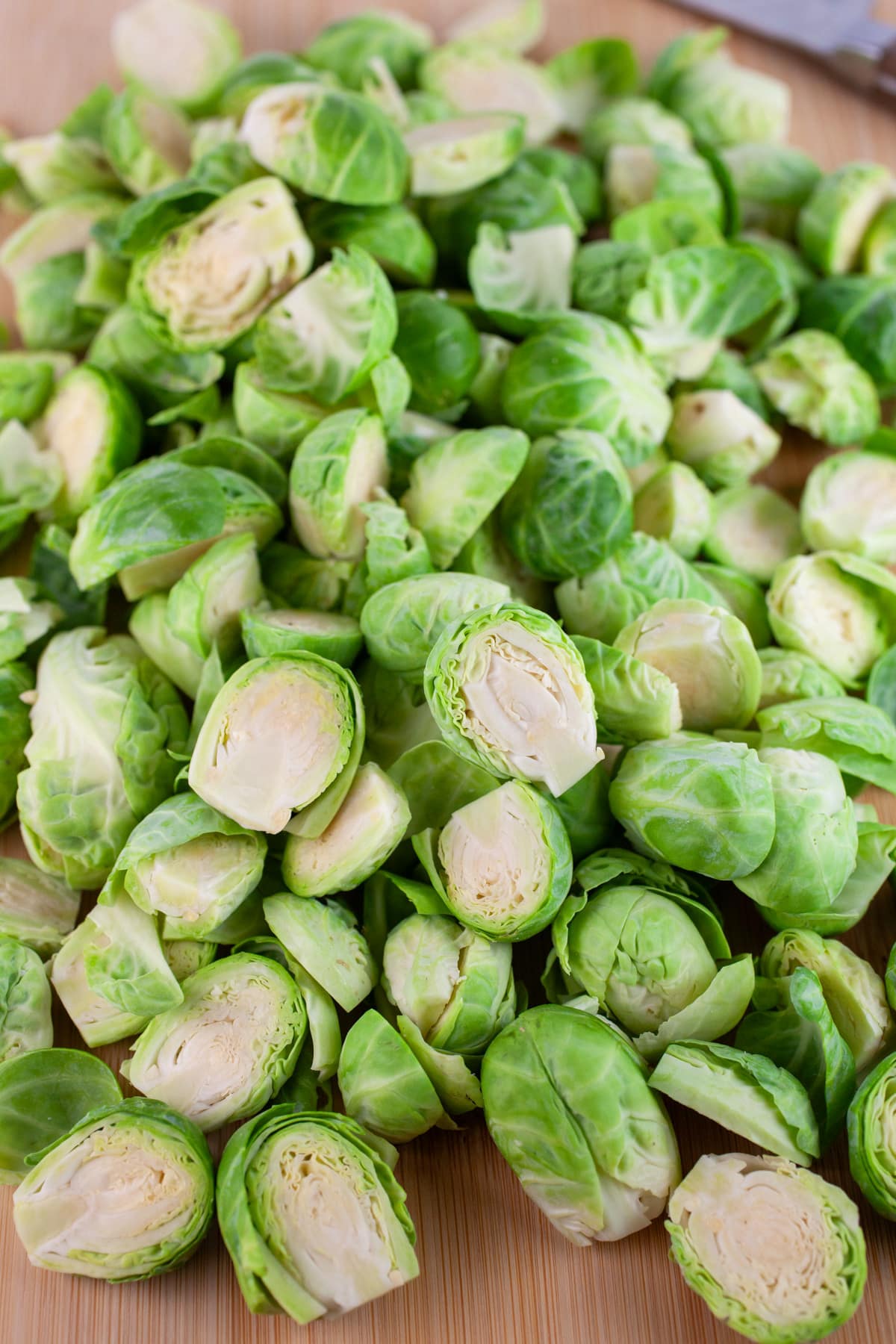 Brussels sprouts cut into halves on wooden cutting board with knife.