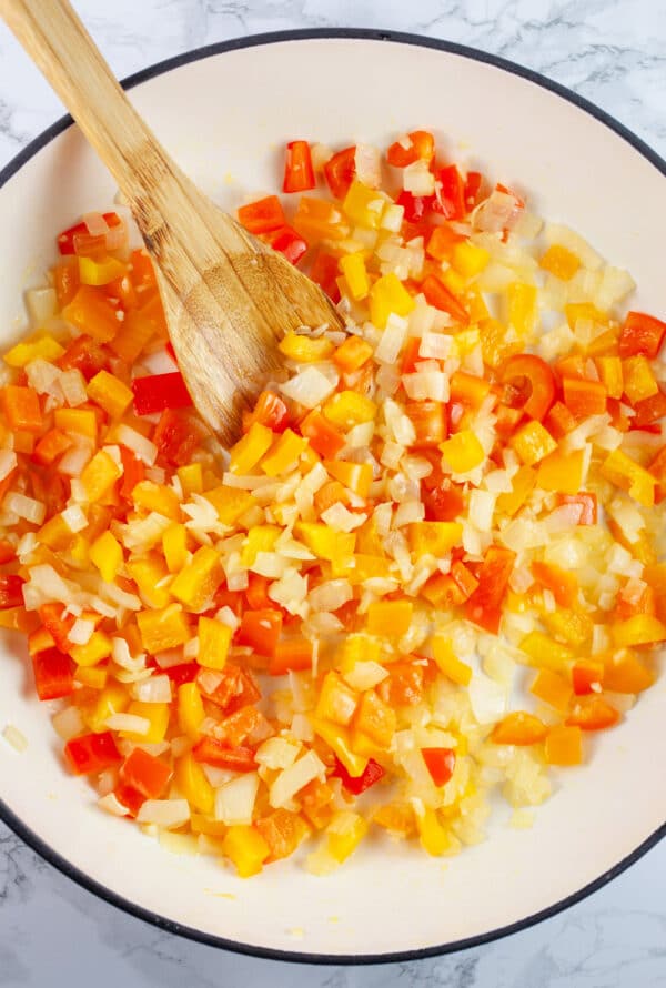 Minced garlic and diced red and orange bell peppers sauteed in Dutch oven with wooden spoon.