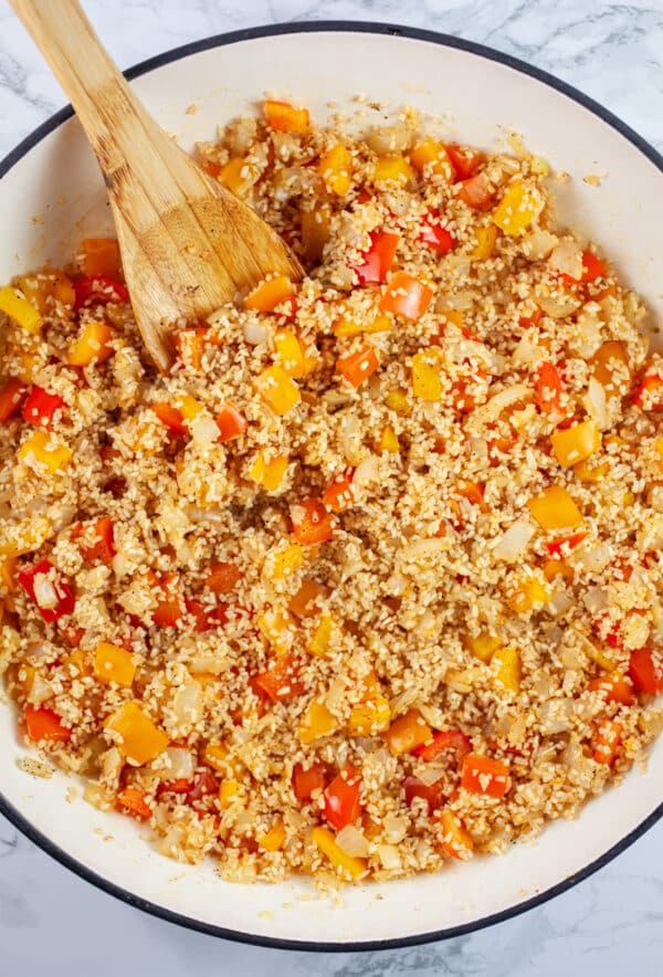 Garlic, red and orange bell peppers, and rice sauteed in Dutch oven with wooden spoon.